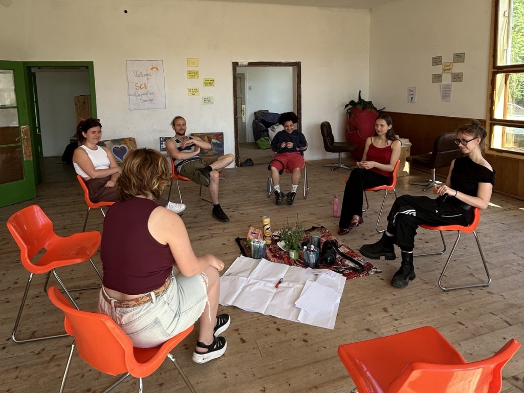 A photo of Amalya Harutyunyan facilitating a session on accessibility. Five participants sit in a circle of chairs listening to her speak.
